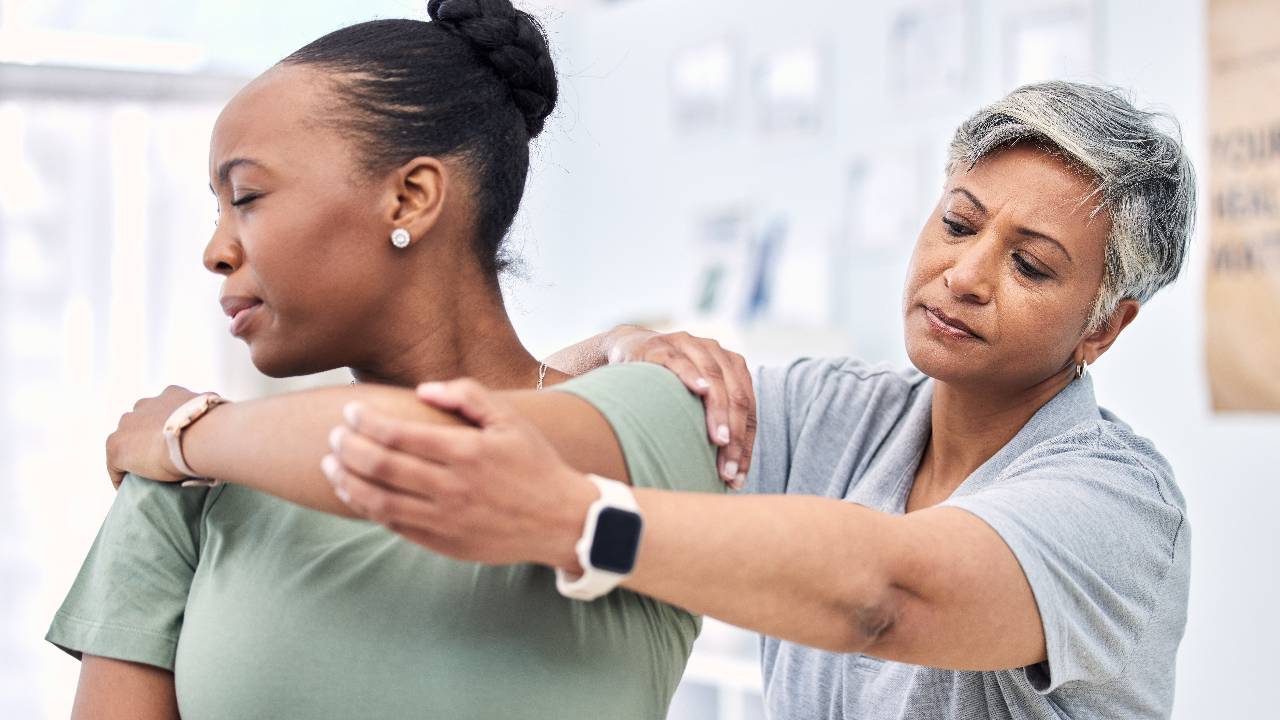 Shoulder pain, physical therapy and chiropractor with patient, injury and healthcare with help and women at clinic.